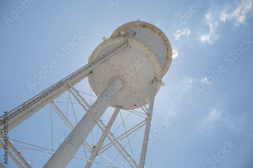 Looking up at a bright white water tower from below backlit with the sun and a bright blue sky. photo