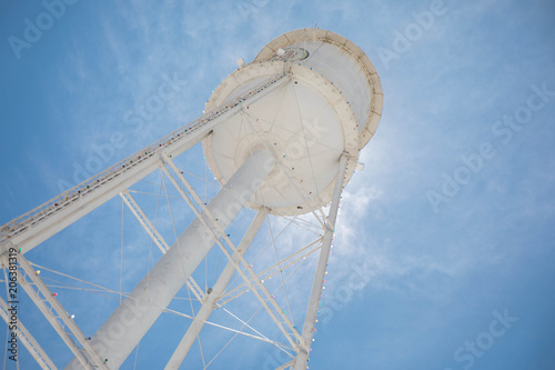 Looking up at a bright white water tower from below backlit with the sun and a bright blue sky. photo