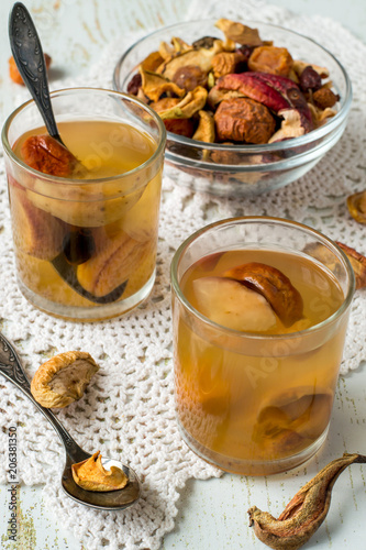 
  A mixture of dried fruits in a small round glass bowl, next to two glasses with compote on an old table. Delicious and healthy drink. 