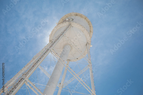 Looking up at a bright white water tower from below backlit with the sun and a bright blue sky. photo