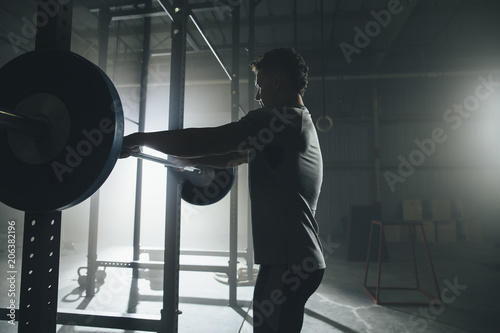 Side view of male athlete lifting barbell at gym