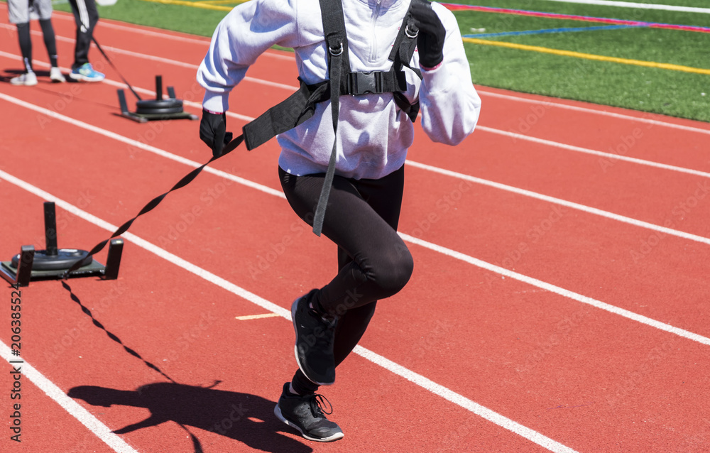 Fototapeta premium High school girls running toward camera pulling a sled with weights