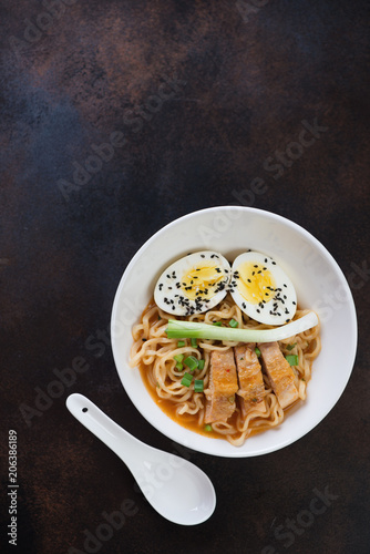 White bowl with chicken ramen noodles, flat-lay over dark brown metal background, vertical shot with copyspace