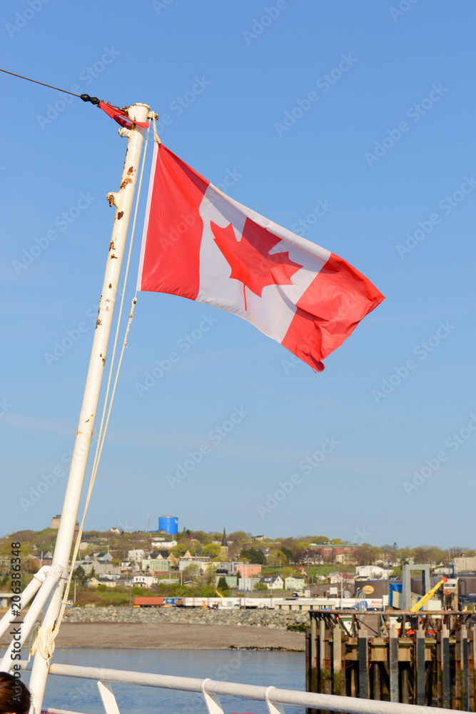 Fototapeta premium Canada national flag on blue sky. Photo taken on the ferry across Bay of Fundy from Saint John, NB to Digby, NS in Atlantic Canada.