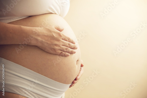 Young pregnant woman holds her hands on her swollen belly. preparation and expectation concept. close-up. horizontal with copy space