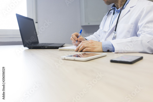 young doctor at the office writing on notebook. Laptop  tablet and mobile phone on the table. Medical concept