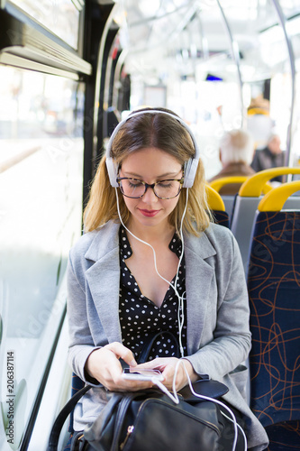 Pretty young woman listening to music with mobile phone at the bus. photo