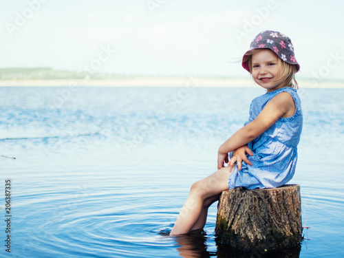 The girl is standing on a stump in the lake.