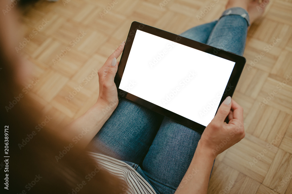 Girl holding empty copy space tablet while sitting on wooden floor. Girl holding empty copy space tablet while sitting on wooden floor.