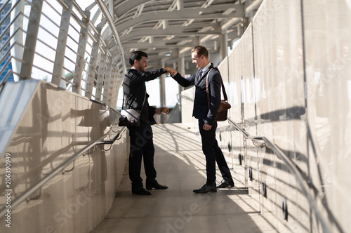 Smiling two Businessman talk and holding coffee make fist bump on the city of the walk way photo