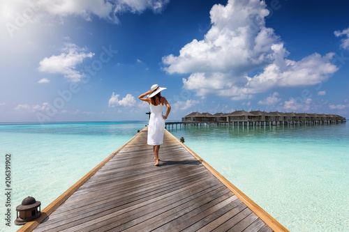 Attraktive Frau in weißem Kleid läuft auf einem Holzsteg auf den Malediven