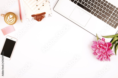 Top view of female worker desktop with laptop, flowers and different office supplies items. Feminine creative design workspace.