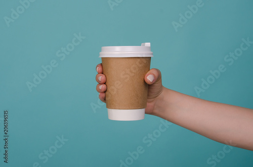 Coffee cup in woman hand isolated on blue background. Female hand with paper cup. Mockup of female hand holding a coffee paper cup. Copy space