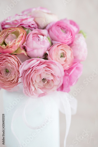 Photograph of a bouquet of sherbet colored ranunculus in a white vase 