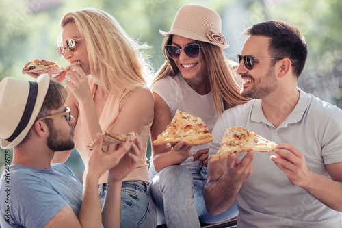 Four cheerful friends sharing pizza outdoor