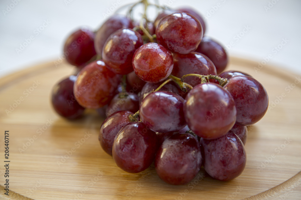 Bunch of ripe red grape on a round bamboo board. Closeup. Bunch of ripe red grape on a round bamboo board. Closeup.