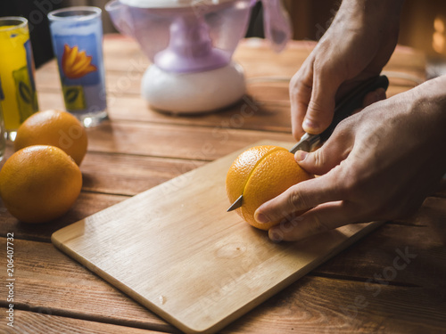 hand cutting fresh oranges with knife on a wooden surface to make juice smoothie
