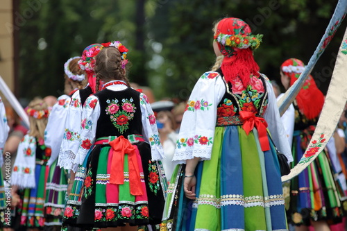 Dziewczyny ubrane w odświętne ludowe stroje łowickie idą w tradycyjnej procesji podczas święta Bożego Ciała, widok z tyłu, kolorowe stroje, słonecznie