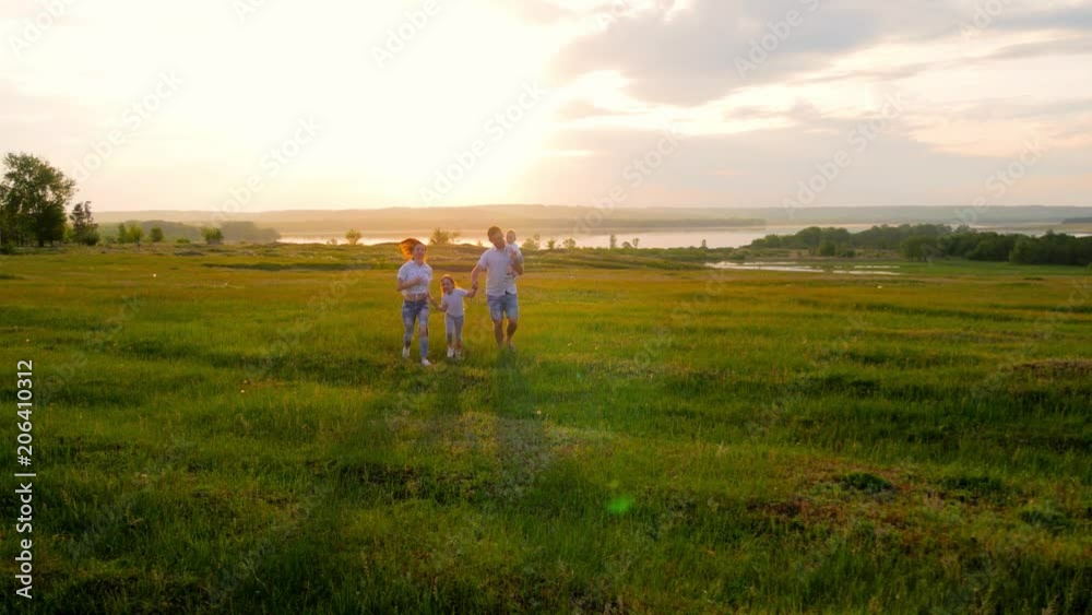 Happy Young Family with two children running on summer field. Healthy mother, father and little children enjoying nature together, outdoors at sunset. Happy Young Family with two children running on summer field. Healthy mother, father and little children enjoying nature together, outdoors at sunset.