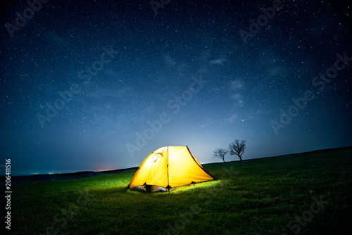 Glowing camping tent in the night mountains under a starry sky