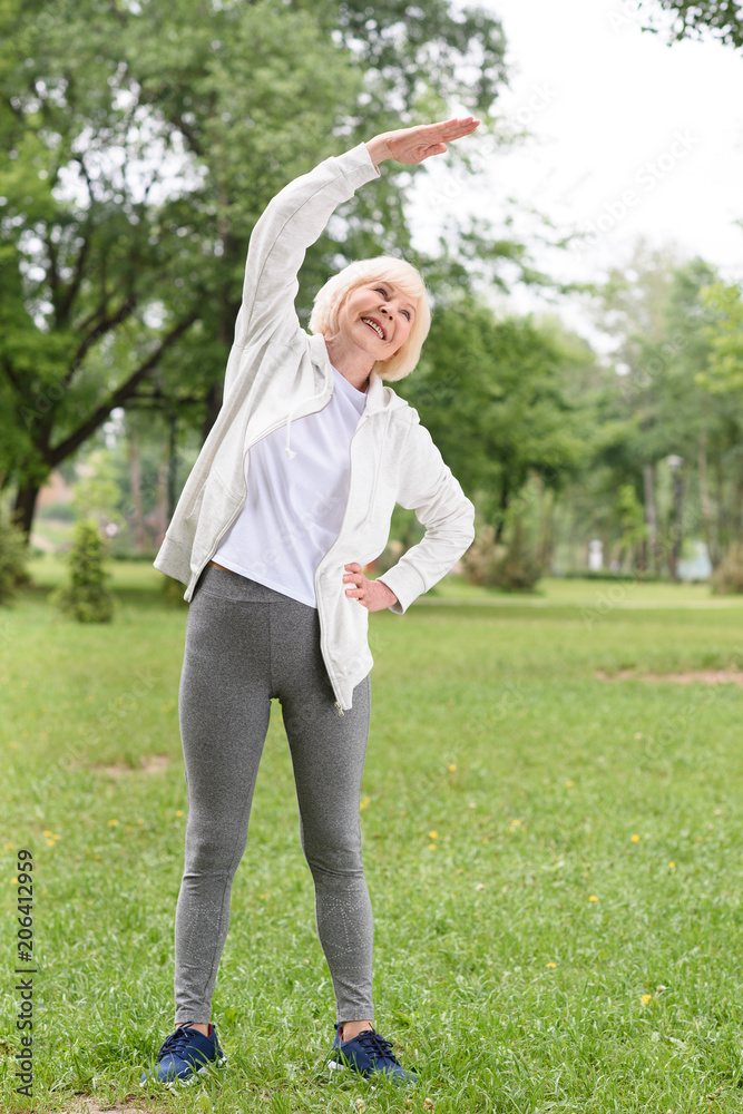 Fototapeta premium elderly sportswoman stretching on green lawn in park
