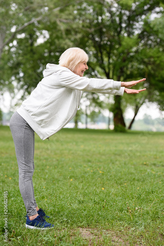 elderly sportswoman exercising on green grass in park, healthy lifestyle