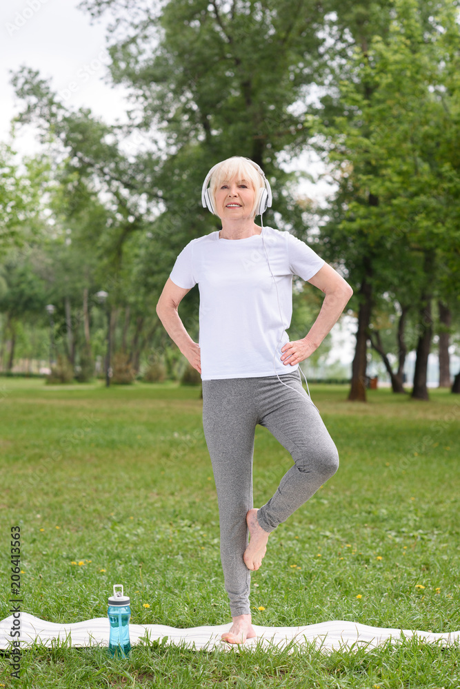 senior female yogi in headphones practicing on yoga mat in park senior female yogi in headphones practicing on yoga mat in park