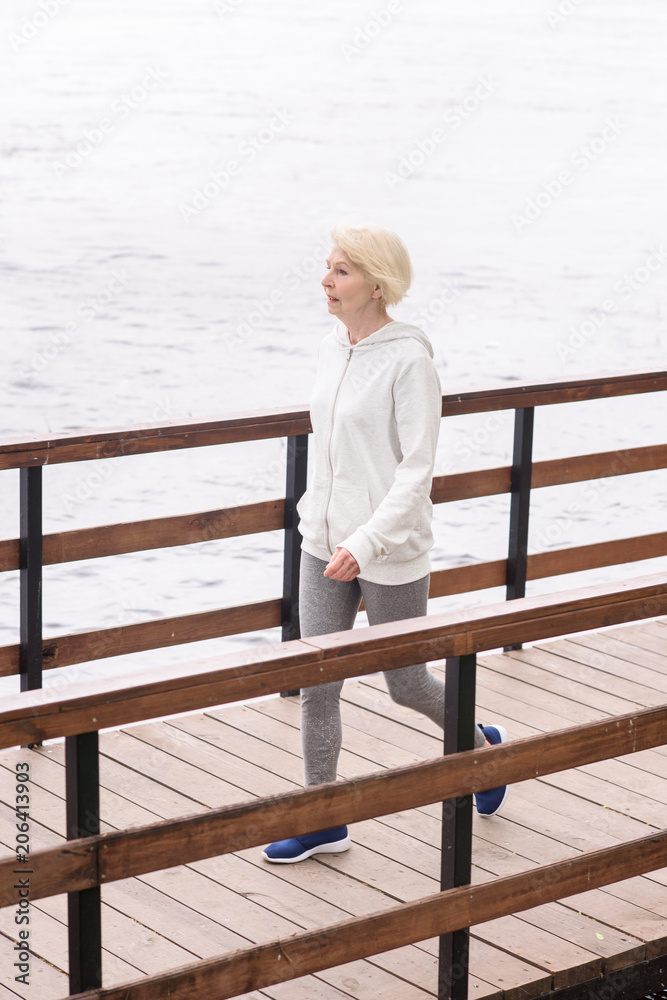 senior woman with grey hair walking on wooden path near river senior woman with grey hair walking on wooden path near river