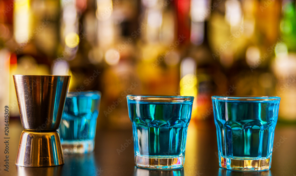 Popular blue drink shot kamikaze on the background of the bar with bottles, a refreshing drink Popular blue drink shot kamikaze on the background of the bar with bottles, a refreshing drink