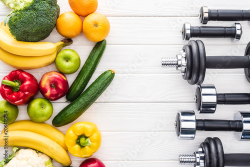 top view of fresh fruits with vegetables and various dumbbells on wooden surface