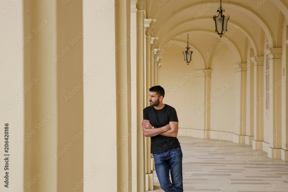 Handsome young man standing outdoors under old colonnade