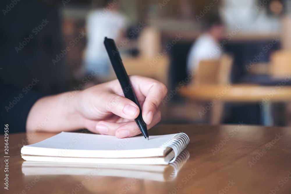 Fototapeta premium Closeup image of a hand writing down on a white blank notebook on table