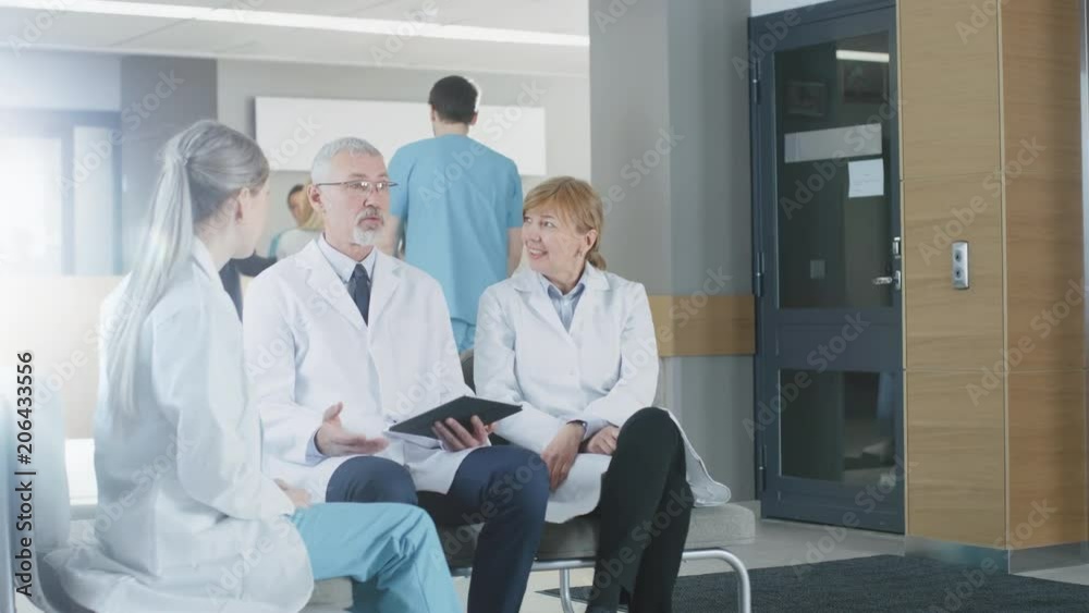 In the Lobby of the Hospital Three Professional Doctor Have Discussion while Sitting. They Use Tablet Computer. Shot on RED EPIC-W 8K Helium Cinema Camera. In the Lobby of the Hospital Three Professional Doctor Have Discussion while Sitting. They Use Tablet Computer. Shot on RED EPIC-W 8K Helium Cinema Camera.