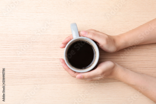 Young woman with cup of delicious hot coffee on wooden background, top view