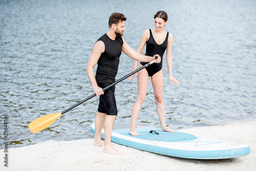 Male coach teaching young woman to row on the standup paddleboard standing on the beach