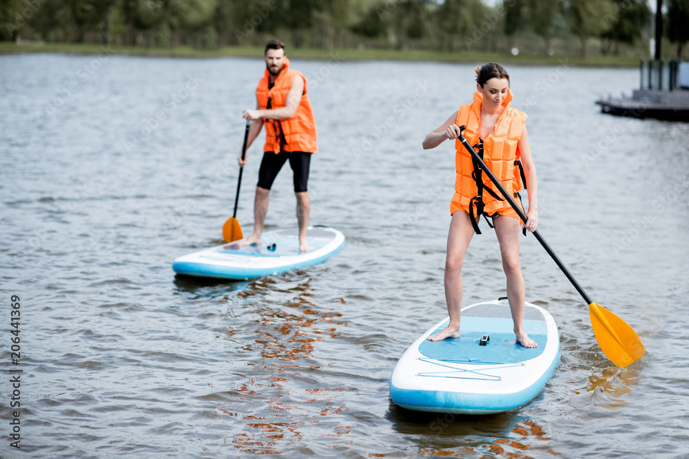 Naklejka premium Couple in life vests learning to row on the stand up paddleboard on the lake