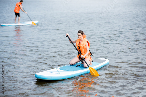 Couple in life vests learning to row on the stand up paddleboard on the lake