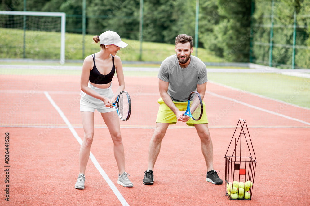 Male instructor teaching young woman to play tennis on the tennis court outdoors