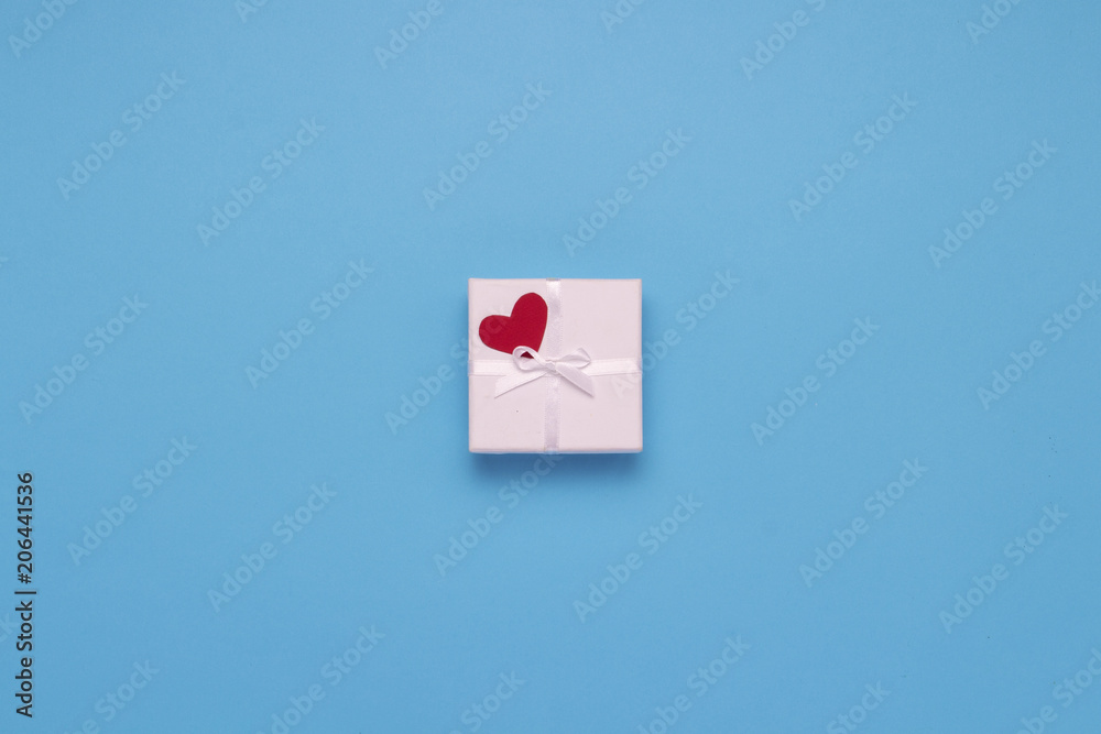 White gift box, red heart on a blue background. Minimalistic style. Concept surprise and suspense, a gift from a loved one. Flat lay, top view White gift box, red heart on a blue background. Minimalistic style. Concept surprise and suspense, a gift from a loved one. Flat lay, top view