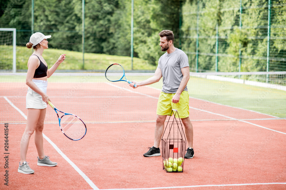 Male instructor teaching young woman to play tennis on the tennis court outdoors