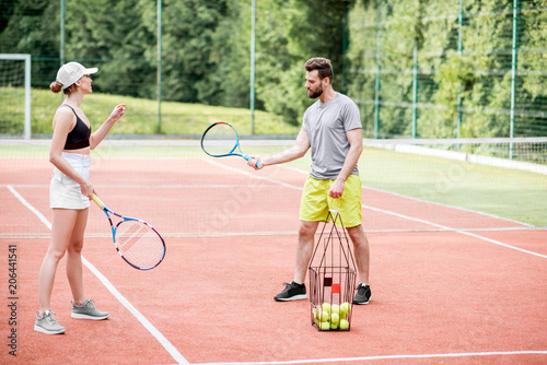Male instructor teaching young woman to play tennis on the tennis court outdoors © rh2010
