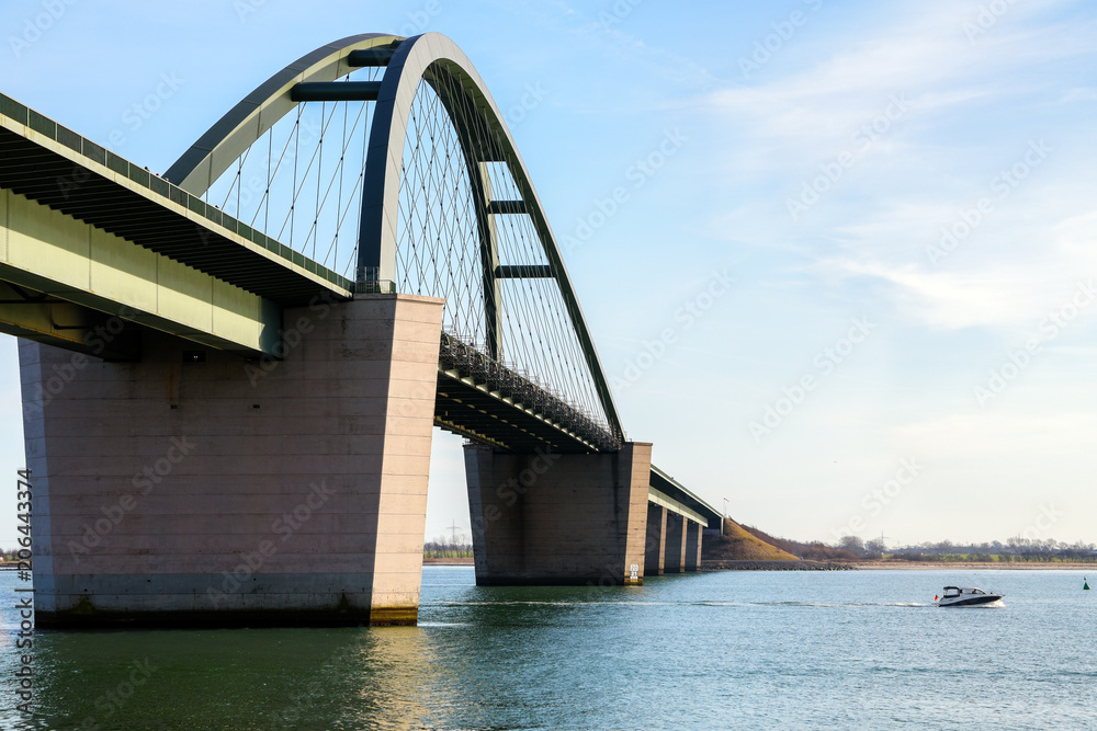 Obraz premium Fehmarn Sound Bridge (German: Fehmarnsundbruecke) and a fast sport boat on the Baltic Sea against a blue sky, vacation travel concept with copy space