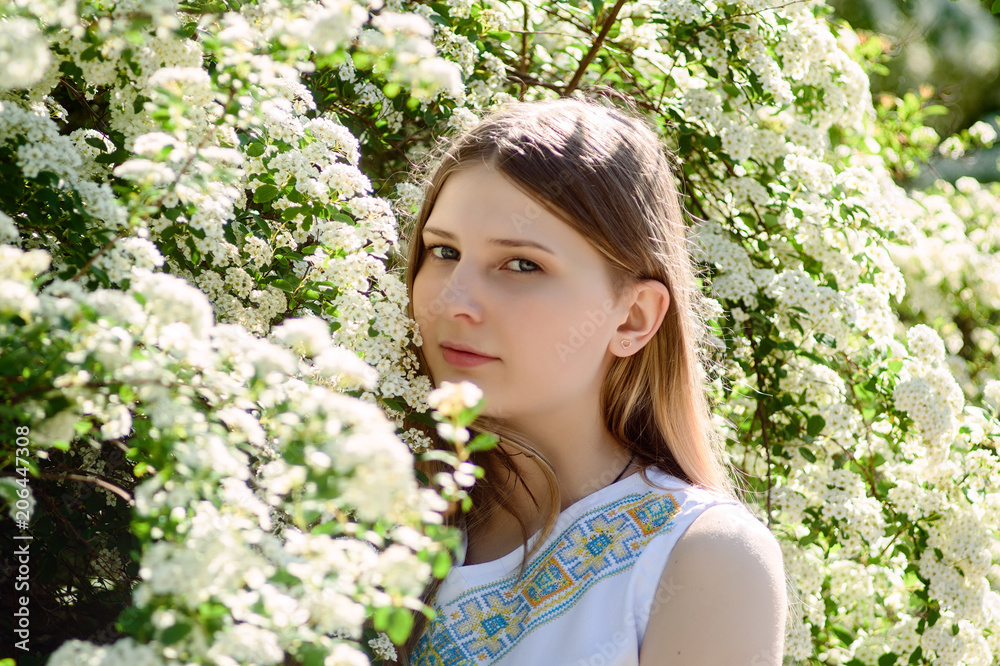 The young girl in white dress stands at the white flowers.