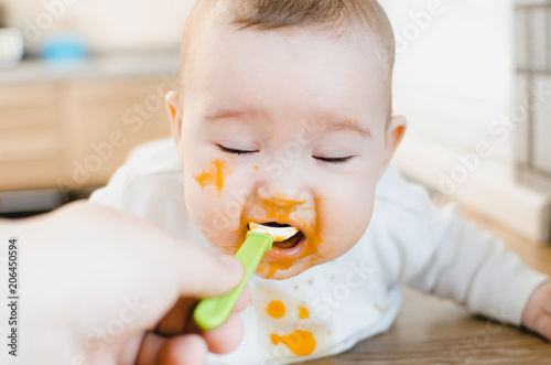 dirty baby in pumpkin puree eats spoon