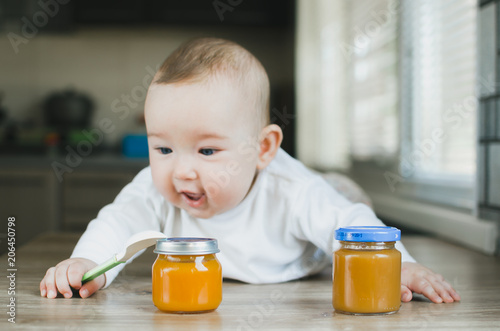 baby with blue eyes crawling, wants to eat pumpkin puree in a jar