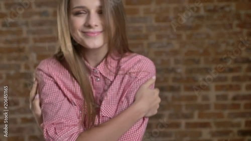 Young cute girl hugs herself, closing eyes, brick background photo