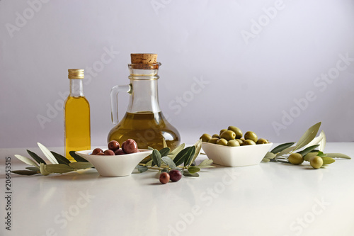 bottle of oil and two bowls of black and green olive isolated on white