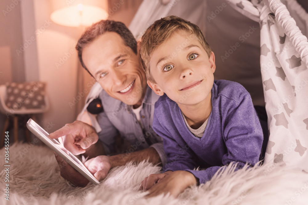 Domestic comfort. Positive cute delighted boy looking at you and smiling while being in the home tent Domestic comfort. Positive cute delighted boy looking at you and smiling while being in the home tent