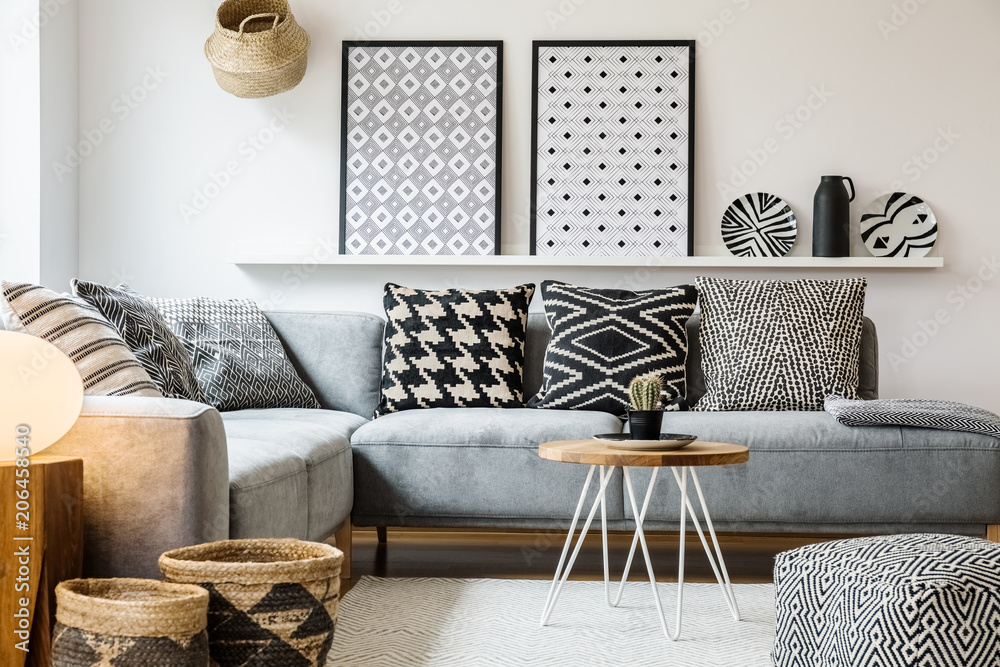 Patterned pillows on grey corner sofa in apartment interior with posters and pouf. Real photo - obrazy, fototapety, plakaty 