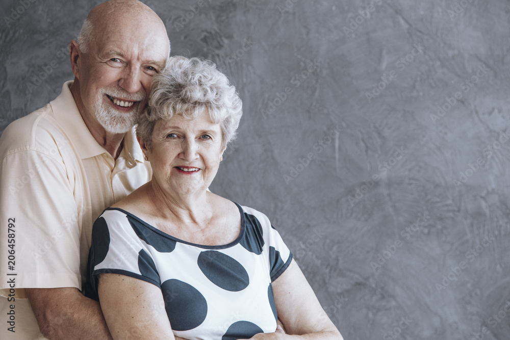 Smiling senior man hugging wife against concrete wall with copy space Smiling senior man hugging wife against concrete wall with copy space